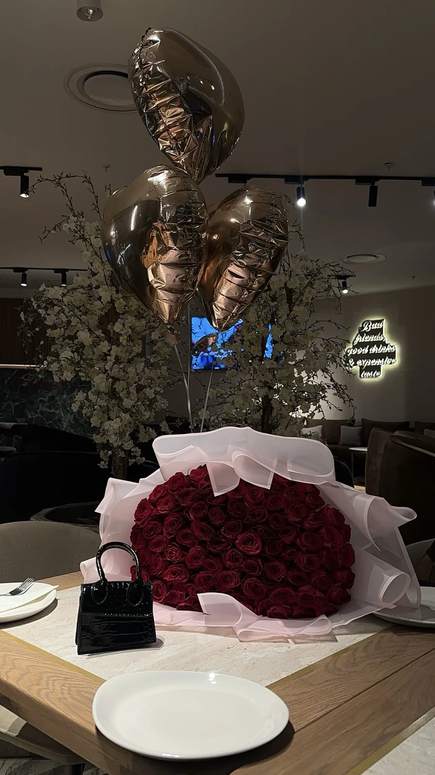 A generous red rose bouquet in pale pink wrapping accompanied by heart balloons