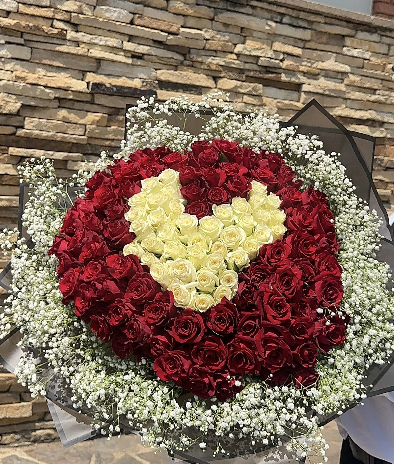 Red roses arranged around an ivory rose heart, framed by baby's breath